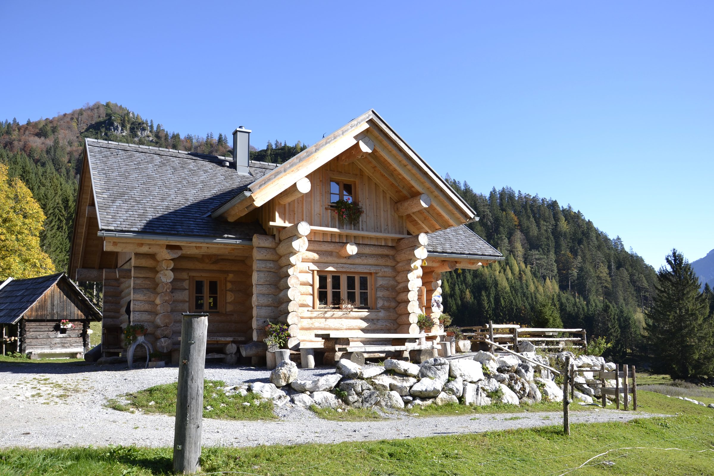 Almhütte aus Rundholz mit Wiese, Wald und Bergen