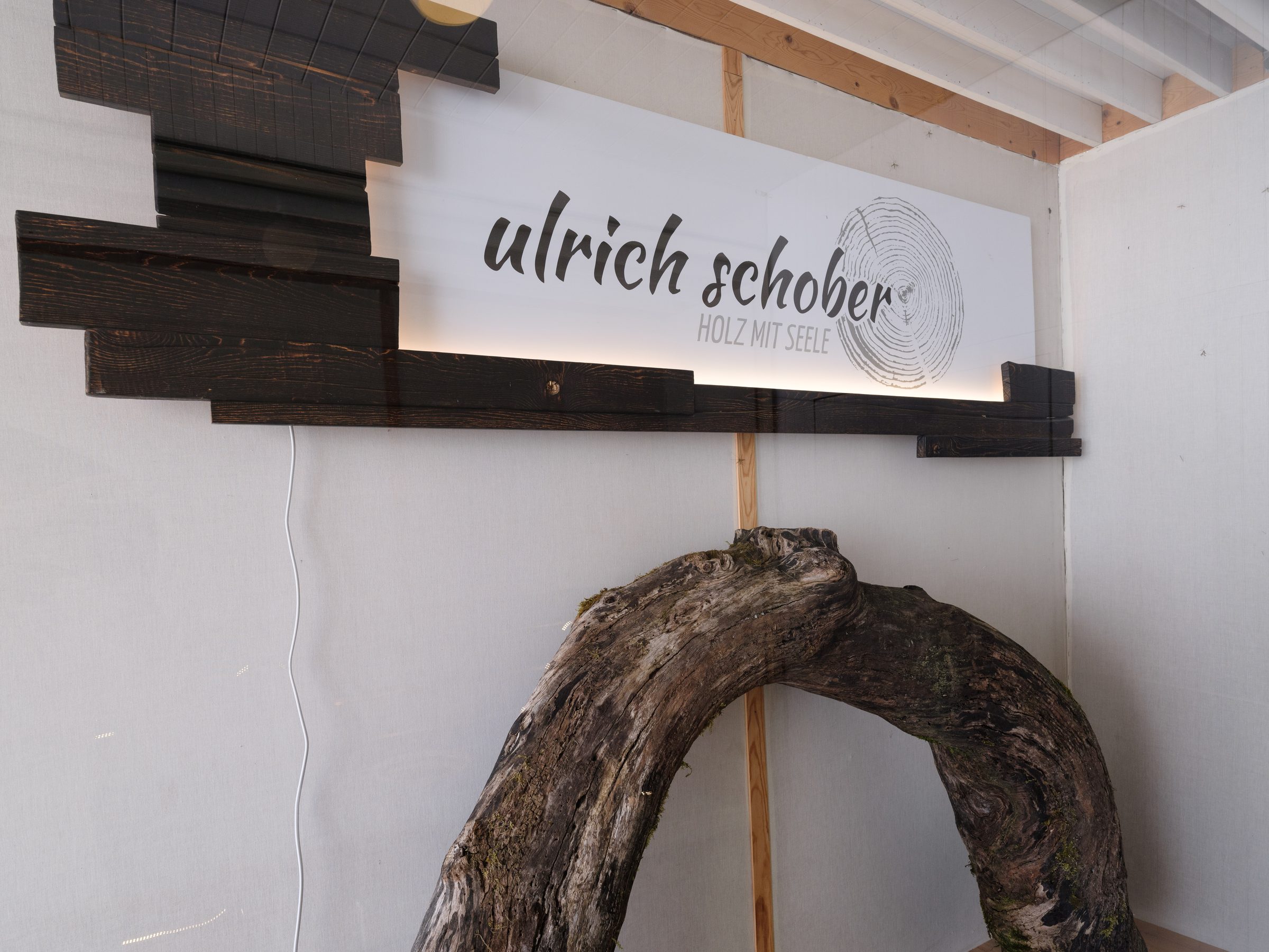 Logo-Wand aus dunklem Holz mit gebogenem Wurzelstück