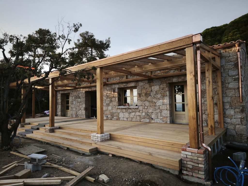 Pergola aus Massivholz mit Terrasse vor einem Steinhaus