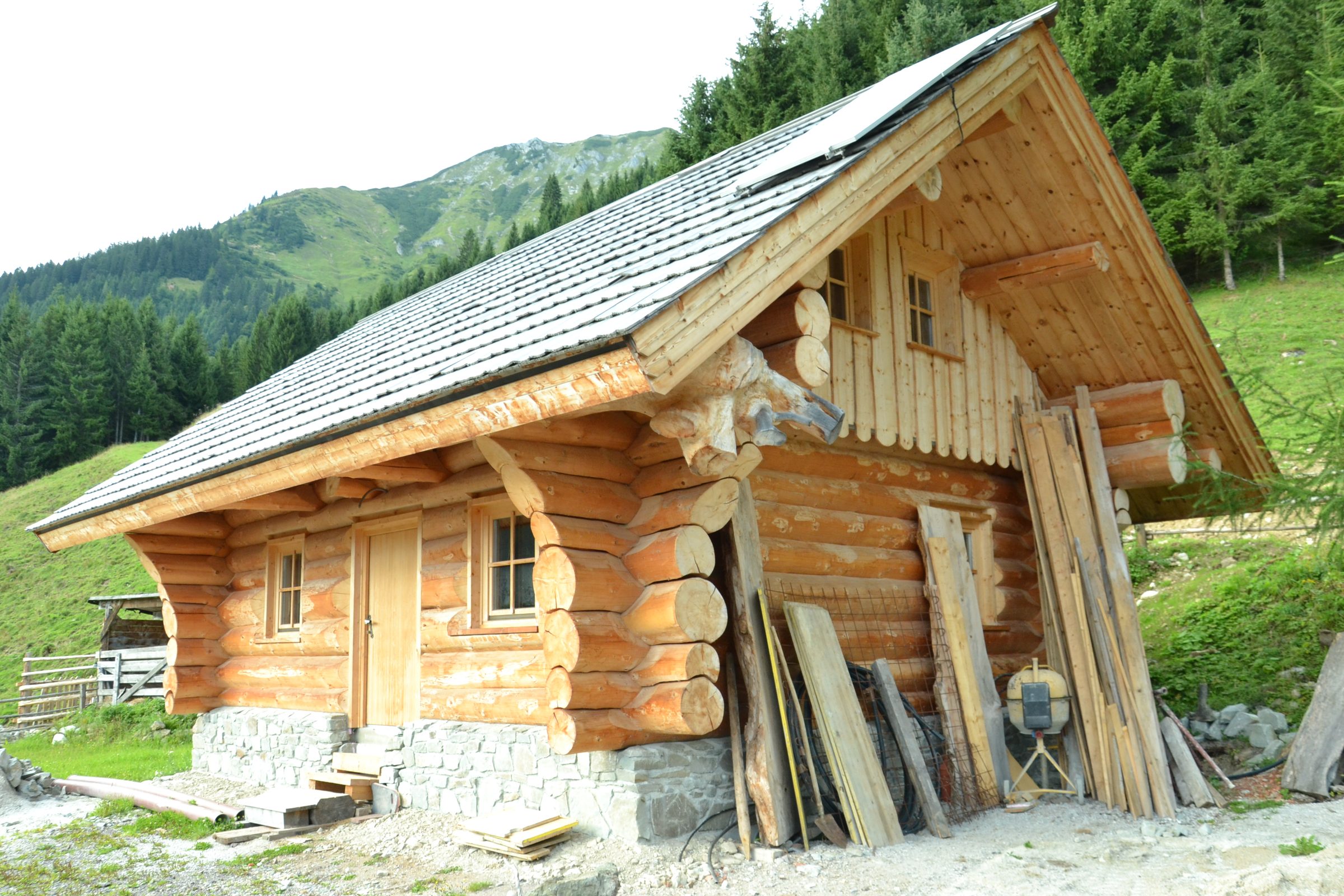 Rundholzhütte mit Schindeldach und Holzstapeln davor