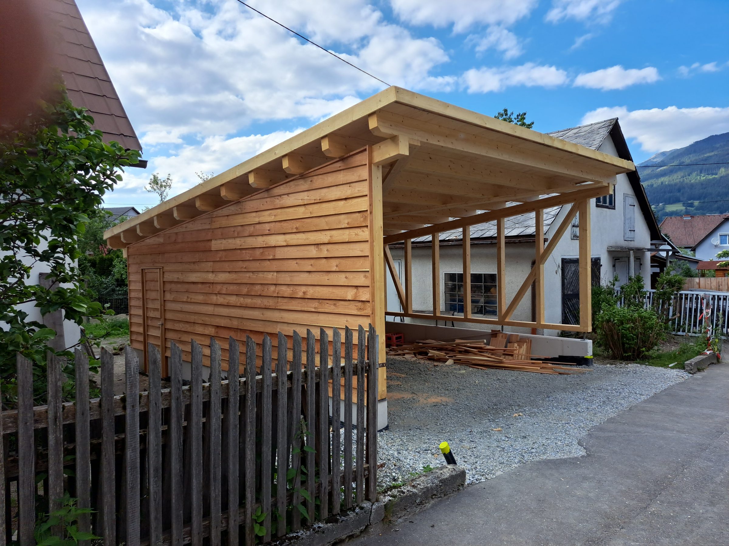 Carport mit Holzschalung und Pultdach hinter einem Holzzaun