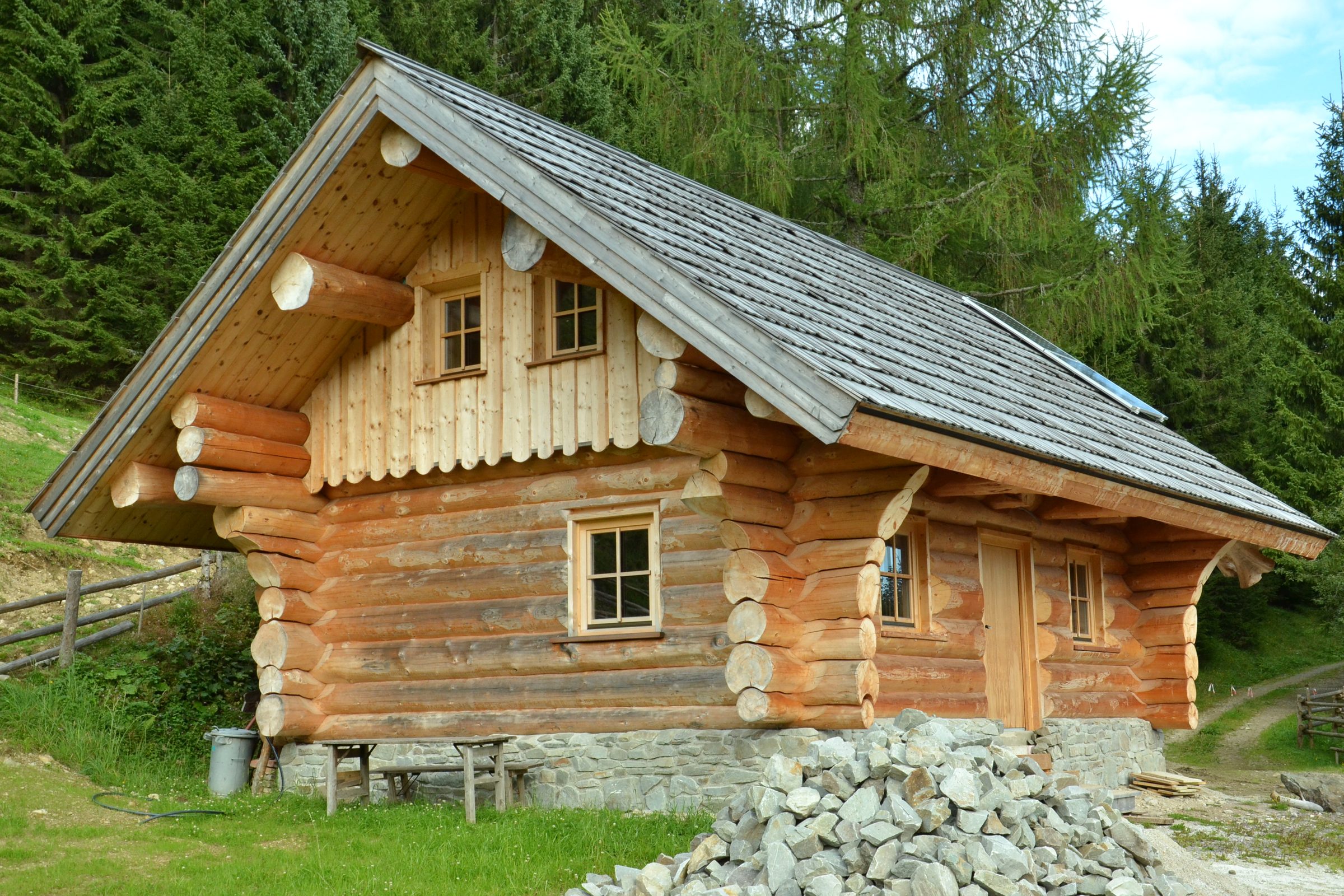 Fertige Rundholzhütte mit Schindeldach auf einer Almwiese
